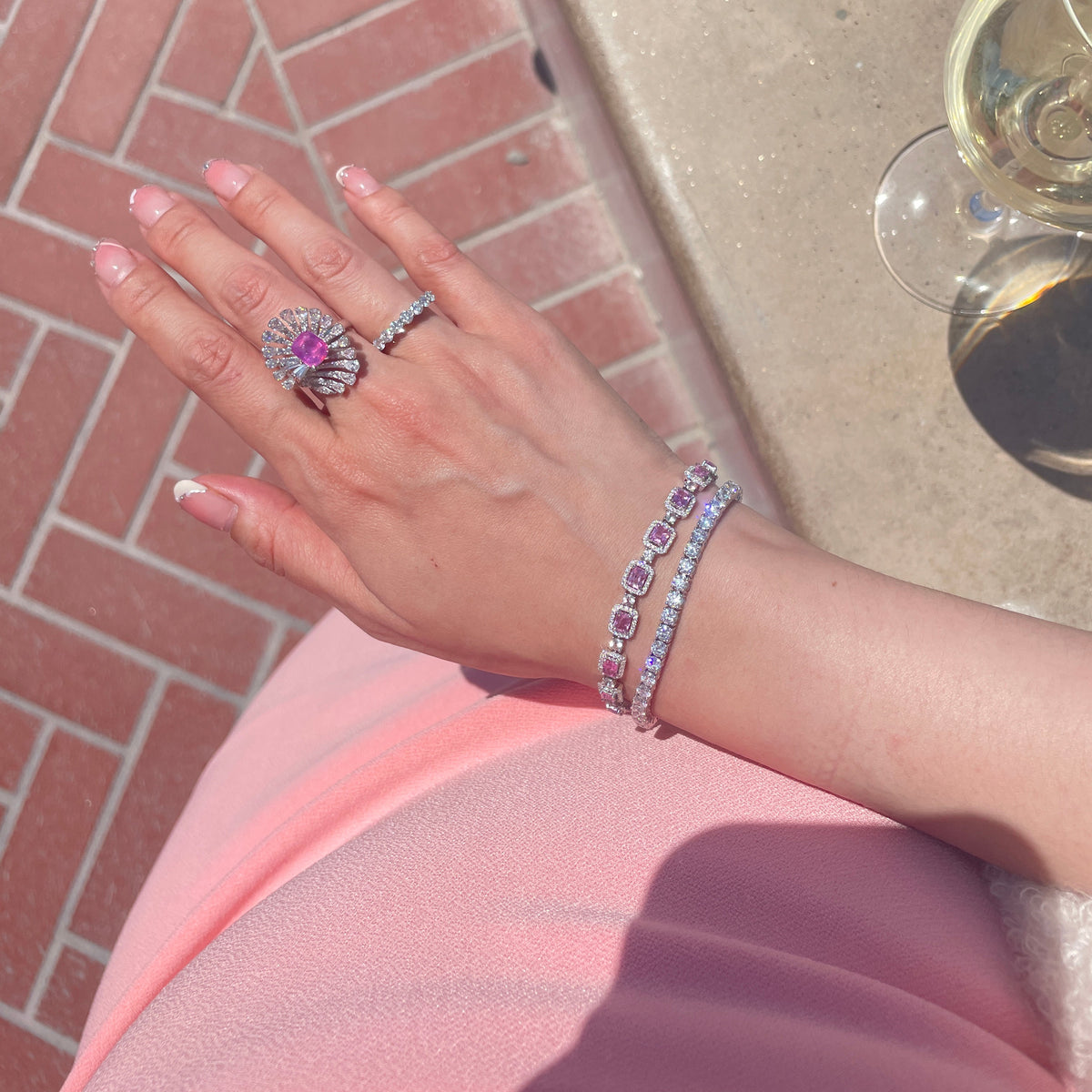 18K white gold tennis bracelet featuring a continuous row of round brilliant-cut diamonds, elegantly styled alongside pink sapphire and diamond jewelry.