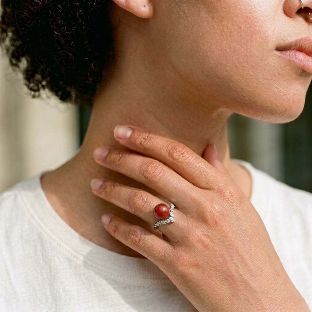Close-up lifestyle shot of a model wearing an 18K white gold ring featuring a round AKA Red Coral cabochon and a curved chevron band of marquise-cut diamonds.