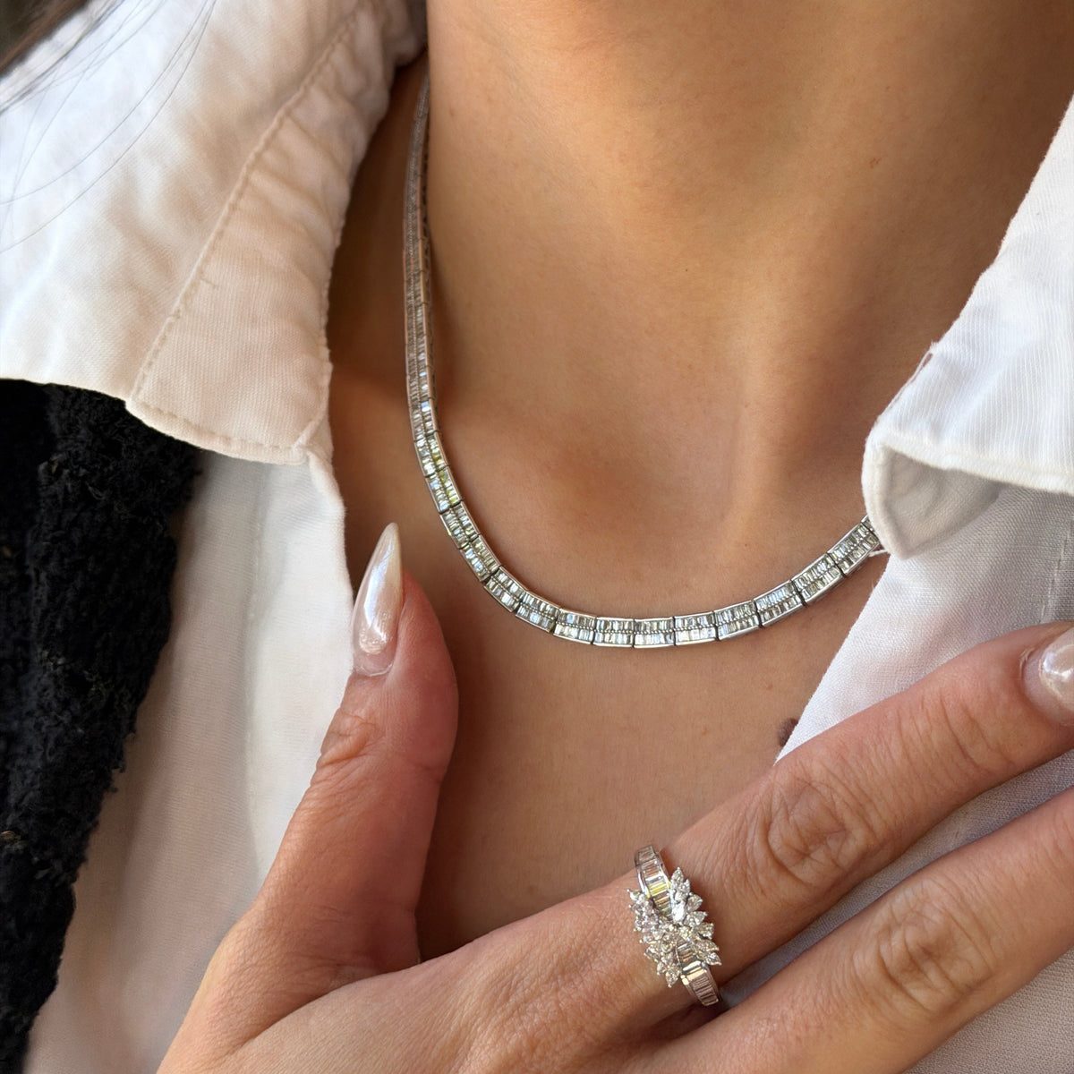 A model showcasing the Baguette Cut Superior Diamond Necklace paired with a matching statement diamond ring. The ring, worn on the hand resting against her white shirt, features a brilliant cluster center and baguette band that perfectly complements the diamond tennis necklace.