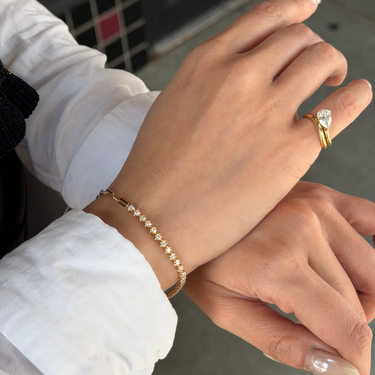 A model showcasing the 18K Natural Diamond Half Paperclip & Tennis Bracelet on her wrist, paired with a stunning pear-shaped diamond ring worn on the hand. The yellow gold jewelry set is styled elegantly against a white collared shirt, perfect for everyday luxury.