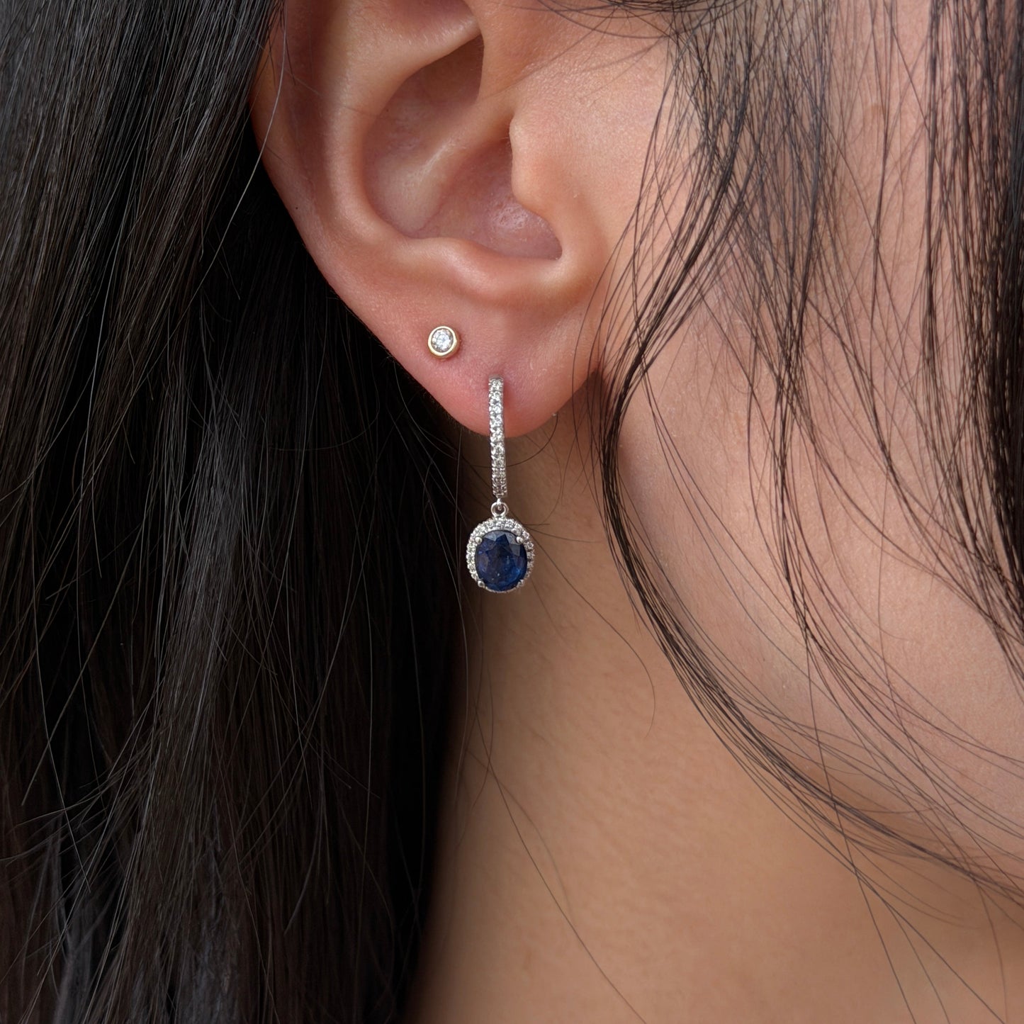 Close up of a woman modeling an 18K white gold natural blue sapphire and diamond halo dangle earring.