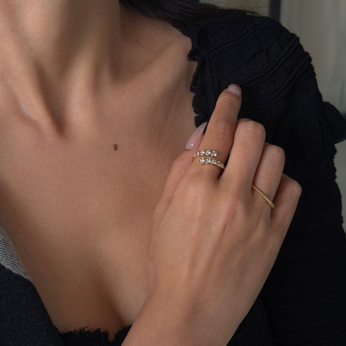 Close-up of a woman modeling an 18K yellow gold open bypass ring with 0.60ctw bezel-set lab-grown diamonds on her index finger.