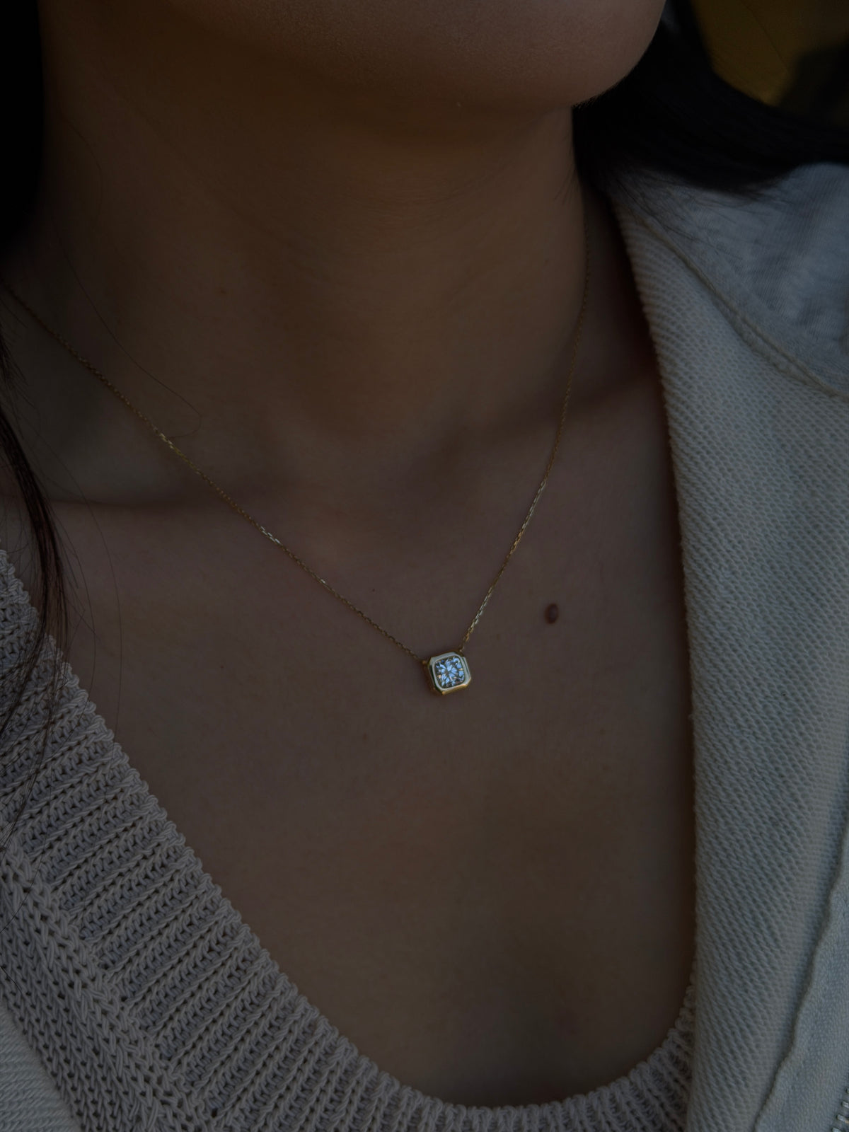 Close-up of a woman wearing an 18K gold bezel set diamond necklace resting elegantly on her collarbone.