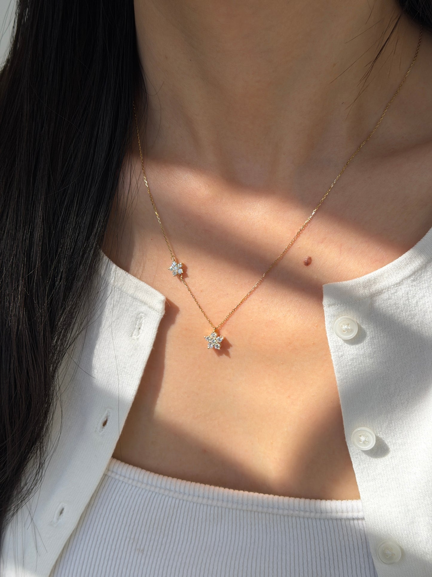 18K yellow gold necklace featuring two asymmetrical diamond-set flower charms on a fine cable chain with an adjustable spring-ring closure.