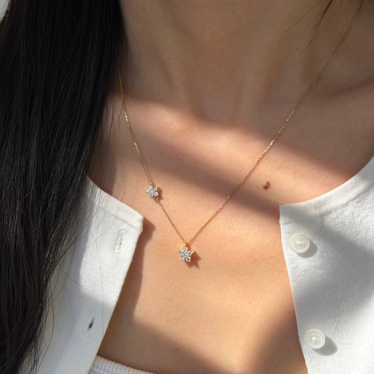 18K yellow gold necklace featuring two asymmetrical diamond-set flower charms on a fine cable chain with an adjustable spring-ring closure.