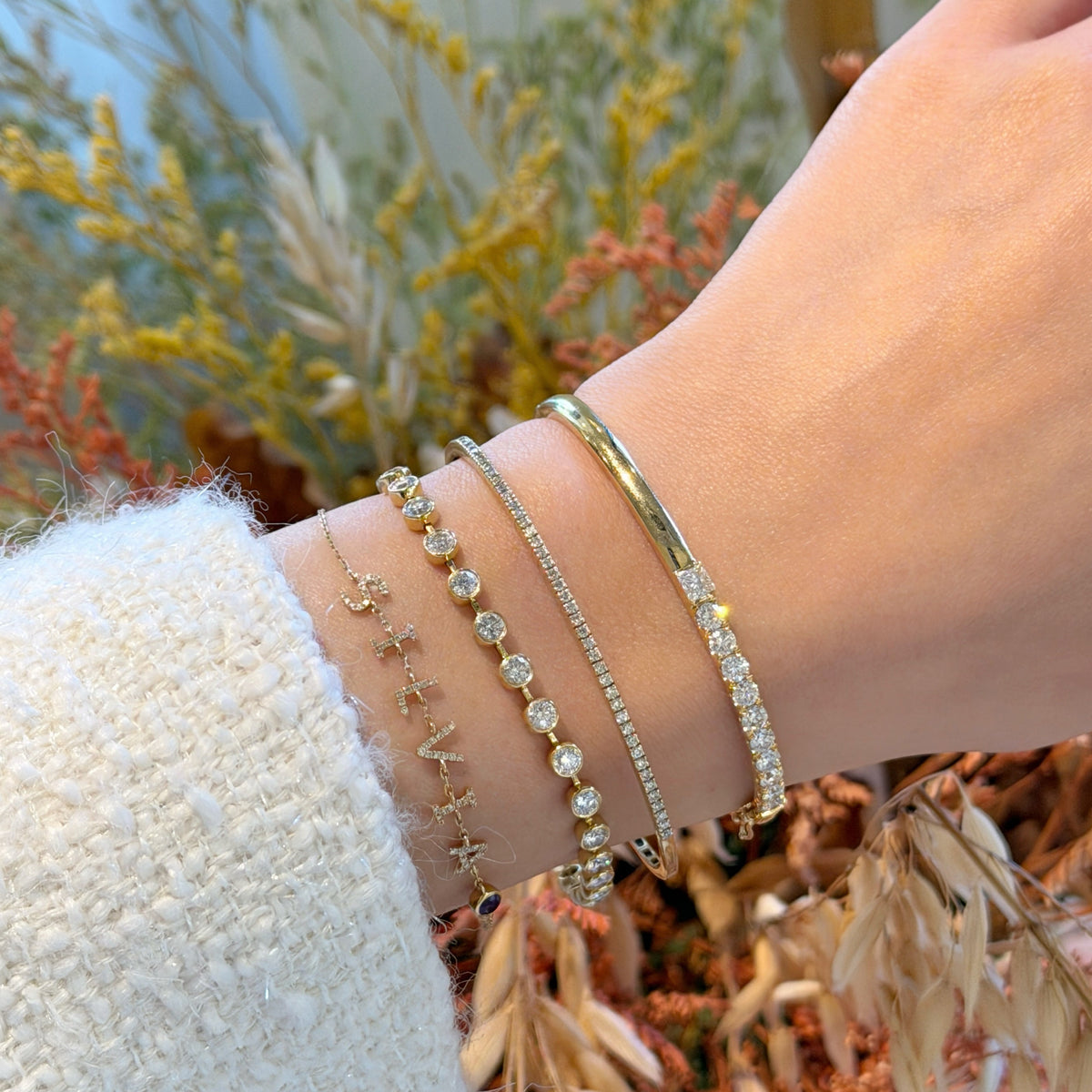 A close-up of a wrist adorned with a sophisticated stack of four gold and diamond bracelets/bangles, featuring the Fantasilvia 18K Half-Eternity Diamond Bangle.