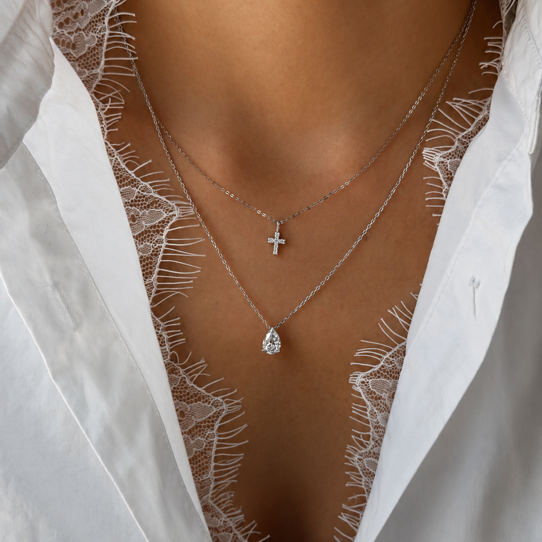 18K white gold mini cross necklace featuring sparkling natural diamonds, styled as a delicate layered necklace with a pear-shaped diamond pendant.