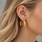 18K yellow gold hoop earrings featuring a bold twisted rope design with sculptural ridges and a polished finish, styled on the ear.