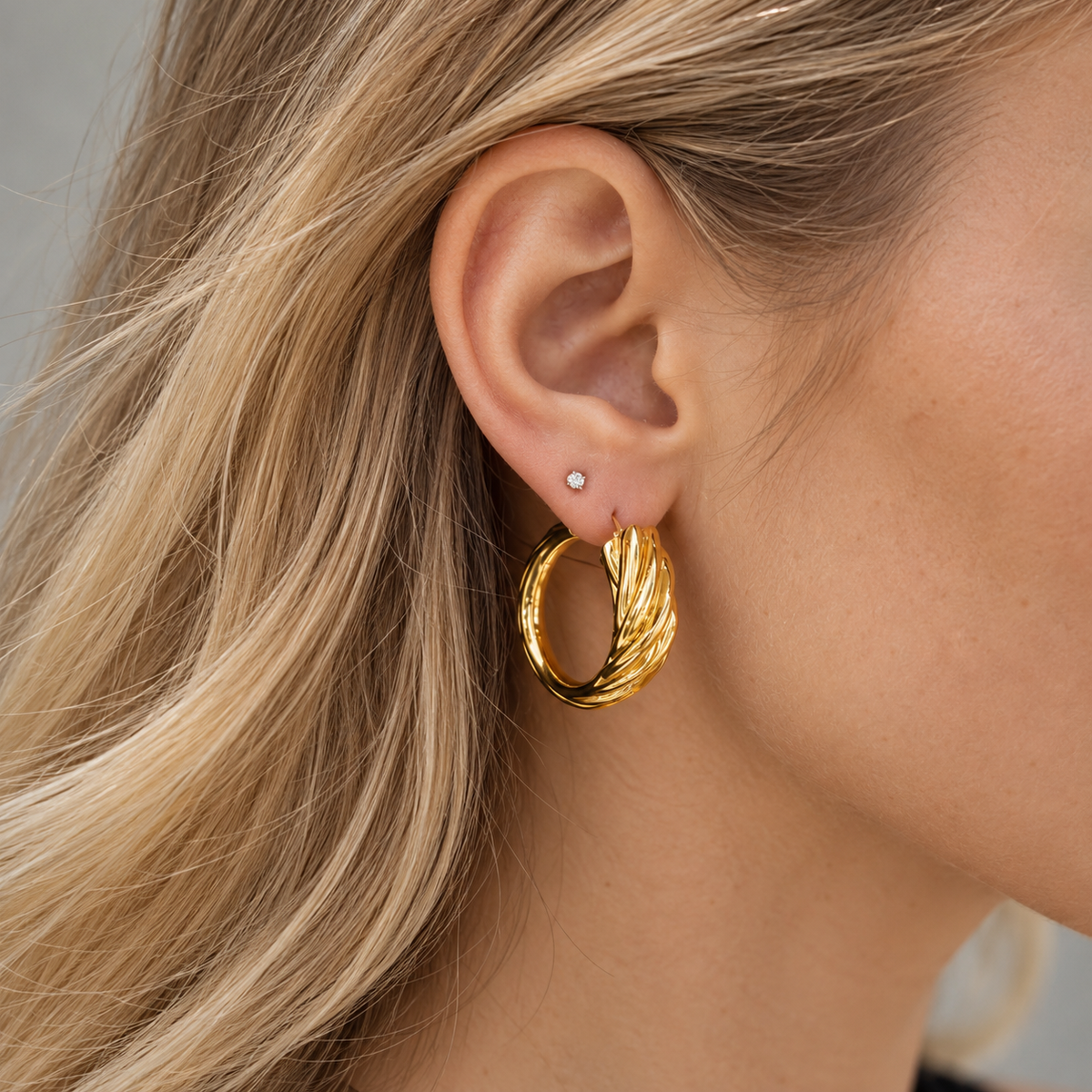 18K yellow gold hoop earrings featuring a bold twisted rope design with sculptural ridges and a polished finish, styled on the ear.