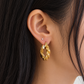 18K yellow gold hoop earrings featuring a bold twisted rope-link design with layered sculptural ridges and a polished finish, styled on the ear.