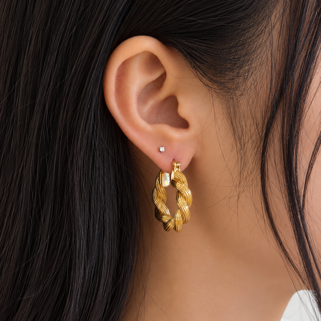 18K yellow gold hoop earrings featuring a bold twisted rope-link design with layered sculptural ridges and a polished finish, styled on the ear.