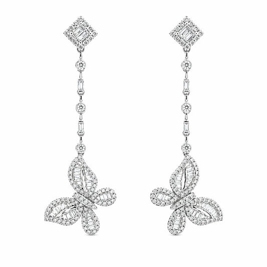 A pair of 18K white gold diamond drop earrings against a white background. Each earring features a diamond-shaped stud, a linear drop chain of alternating round and baguette diamonds, and a detailed butterfly pendant at the base set with a mix of round and baguette-cut diamonds.