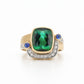 A luxury 18K two-tone gold statement ring featuring an 8.52-carat cushion-cut green tourmaline bezel-set above a pavé diamond crescent, flanked by two cabochon blue sapphires against a white background.