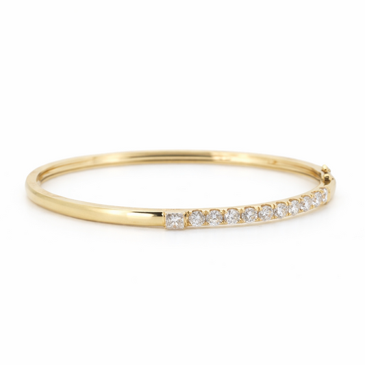 18K yellow gold hinged bangle featuring a row of round brilliant diamonds accented by a princess cut diamond at the terminal.
