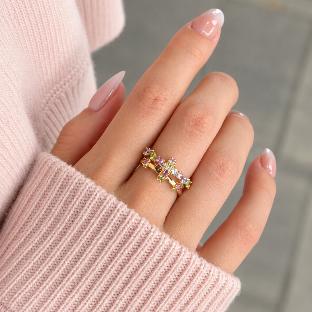 Close-up of The Fairy Garden kinetic ring by Fantasilvia Vancouver, worn stacked on one finger, showcasing a vibrant mix of pink sapphires, aquamarines, and peridots in 18k gold.
