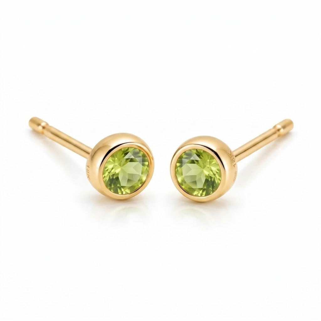 Pair of 18K yellow gold stud earrings featuring bezel-set round light green peridot gemstones.