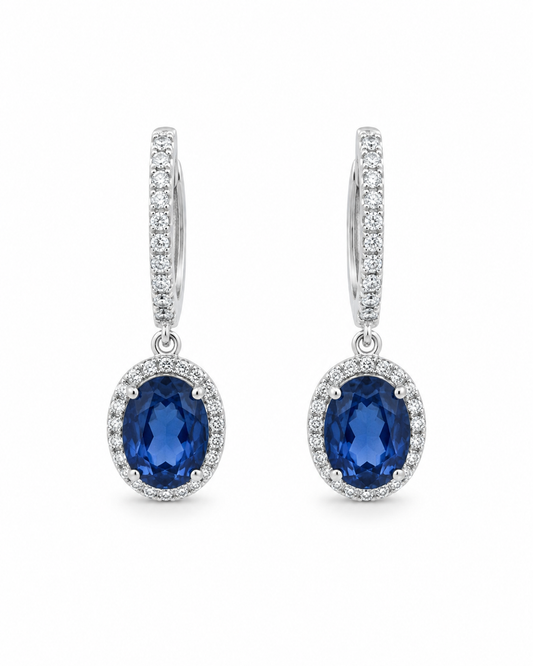 Front view of 18K white gold drop earrings featuring oval natural blue sapphires surrounded by colorless diamond halos on a white background.