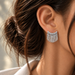 18K white gold fringe earrings featuring a sculptural cascading chain design with textured circular accents, styled on the ear.