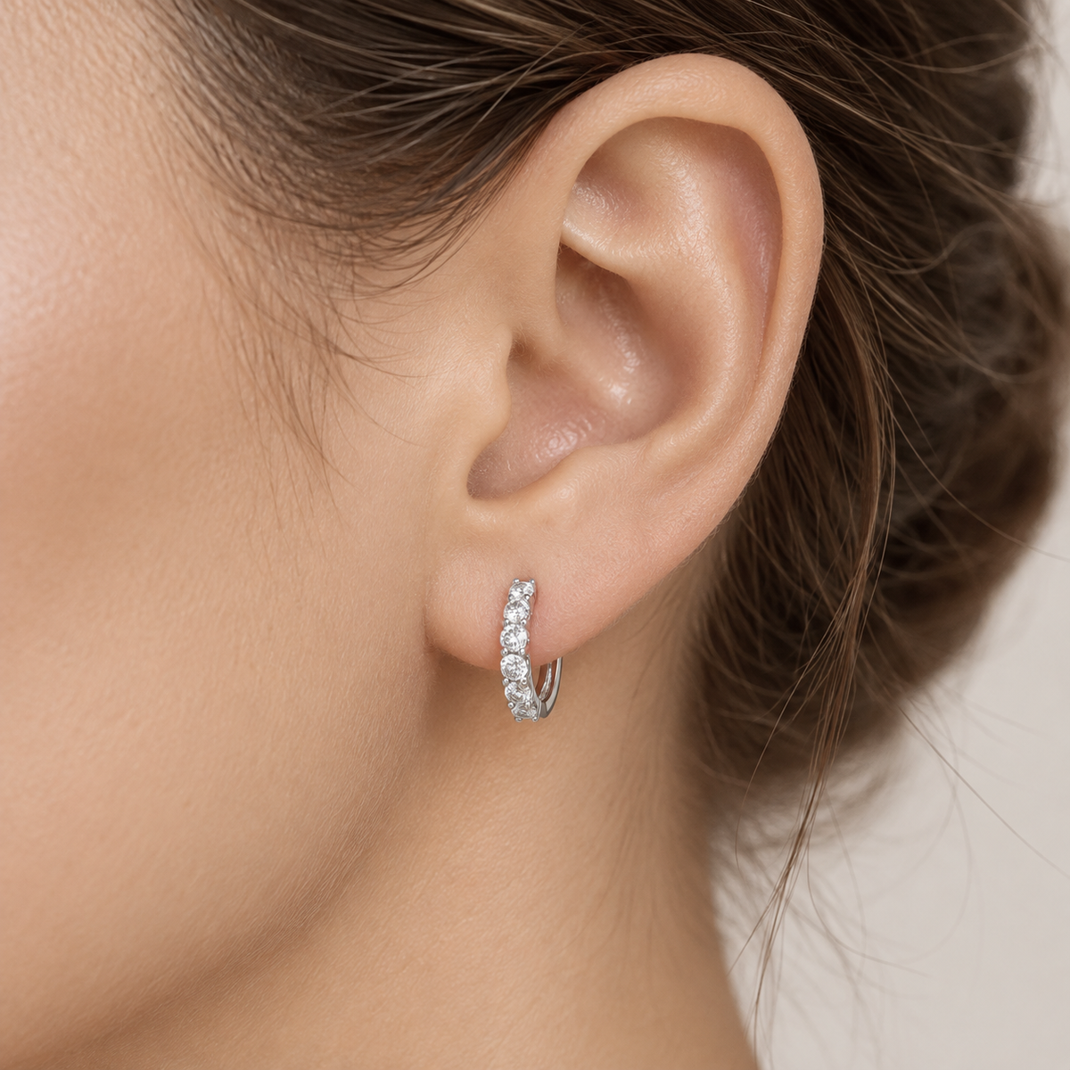 Platinum natural diamond hoop earrings featuring a graduated row of round brilliant-cut diamonds in an elegant prong setting, styled on the ear.