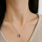 Close-up model shot of a 18k white gold pendant necklace featuring an emerald-cut natural pink tourmaline on a white gold chain, styled on the neck and collarbone with no face shown.