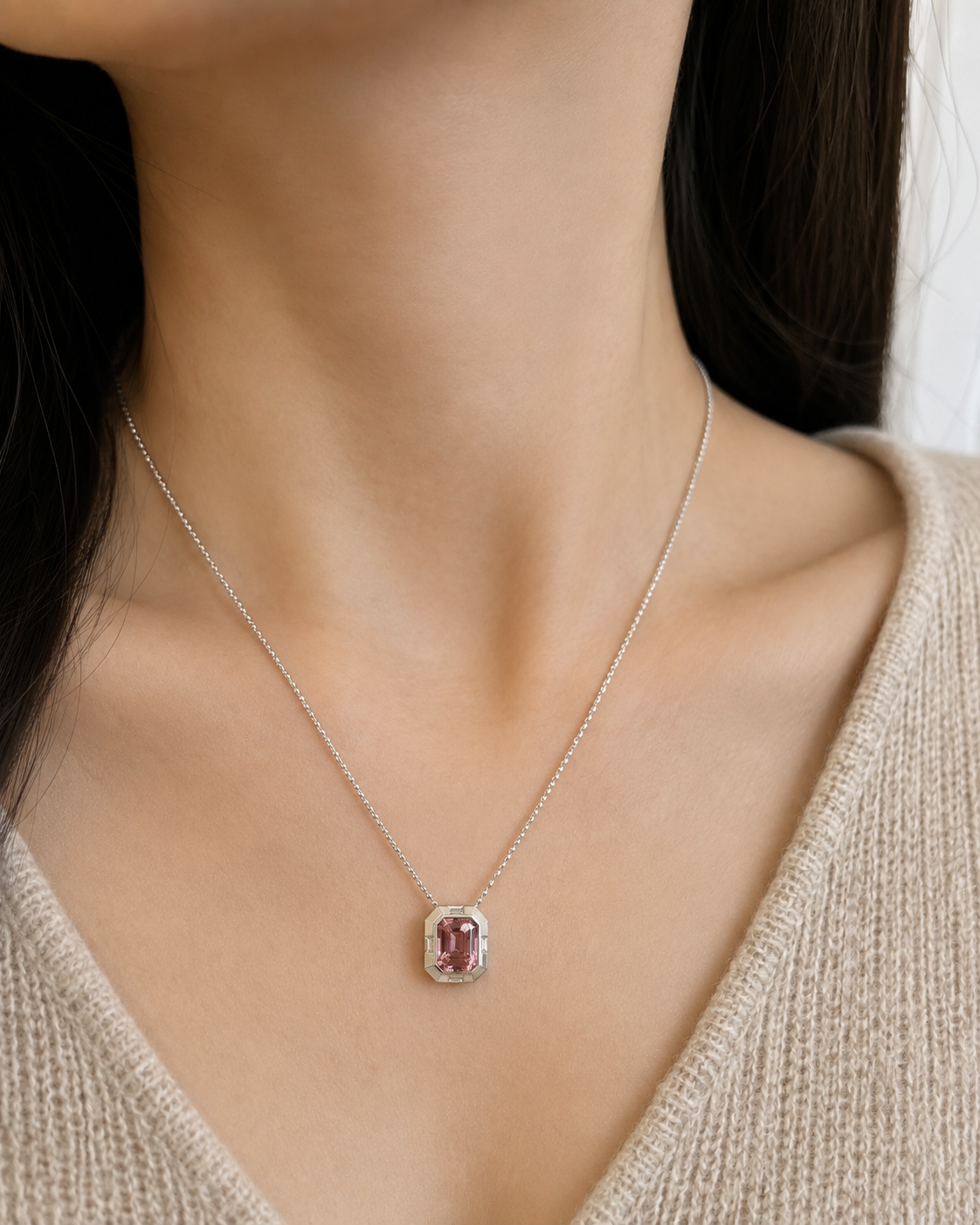 Close-up model shot of a 18k white gold pendant necklace featuring an emerald-cut natural pink tourmaline on a white gold chain, styled on the neck and collarbone with no face shown.