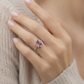 Close-up model shot of a 18k white gold ring featuring an emerald-cut natural pink tourmaline, worn on the hand against a soft beige knit sweater with no face shown.
