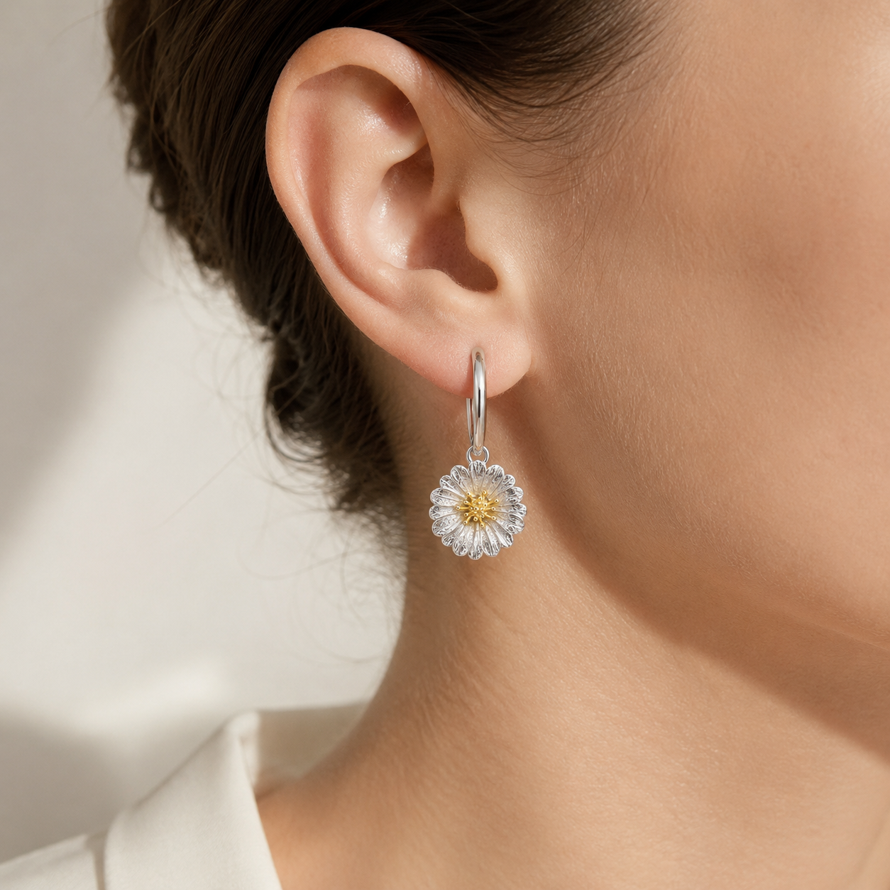 Model wearing the First Bloom daisy drop earring featuring a silver huggie hoop and a two-tone floral charm with 18K gold accents.