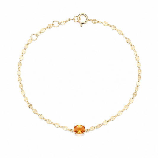 A delicate 18K yellow gold fine jewelry bracelet featuring a small, horizontally set natural fiery orange spessartine garnet center stone on a highly reflective sparkle chain against a solid white background.