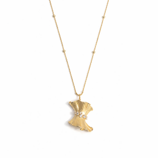 A gold pendant necklace shaped like a flowing gown with a textured finish, featuring a cinched waist accented by a row of small, round-cut diamonds, suspended from a gold station chain on a white background.