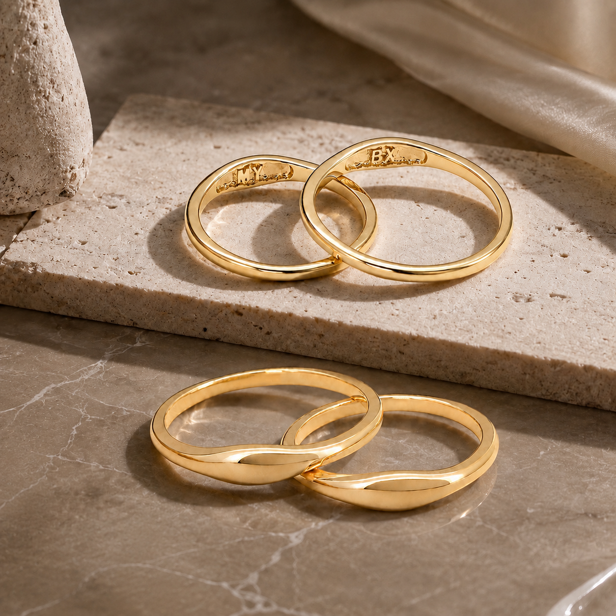 18K gold custom couple rings displayed on a textured stone, beautifully highlighting the secret MY and BX inner band engravings.