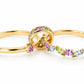 The Fairy Garden custom kinetic ring laid open against a white background. It features two 18k yellow gold bands connected by a movable center loop. The ring is beautifully set with a whimsical, vine-like pattern of green peridots, pink sapphires, and light blue aquamarines in round and marquise cuts.