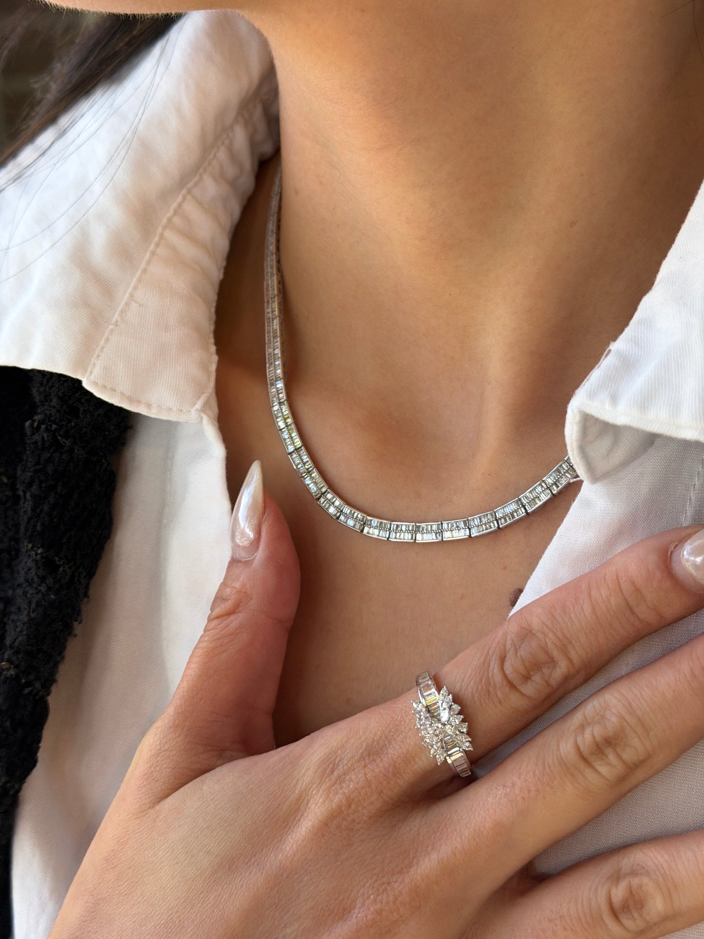 A model showcasing the Baguette Cut Superior Diamond Necklace paired with a matching statement diamond ring. The ring, worn on the hand resting against her white shirt, features a brilliant cluster center and baguette band that perfectly complements the diamond tennis necklace.