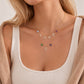 Model wearing layered 14K solid gold Spell My Stars necklaces featuring detachable diamond initial charms and natural birthstone pendants.