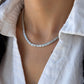 Close-up in IMG_0725.jpg of a woman wearing a sparkling baguette-cut diamond tennis necklace with an open white shirt.