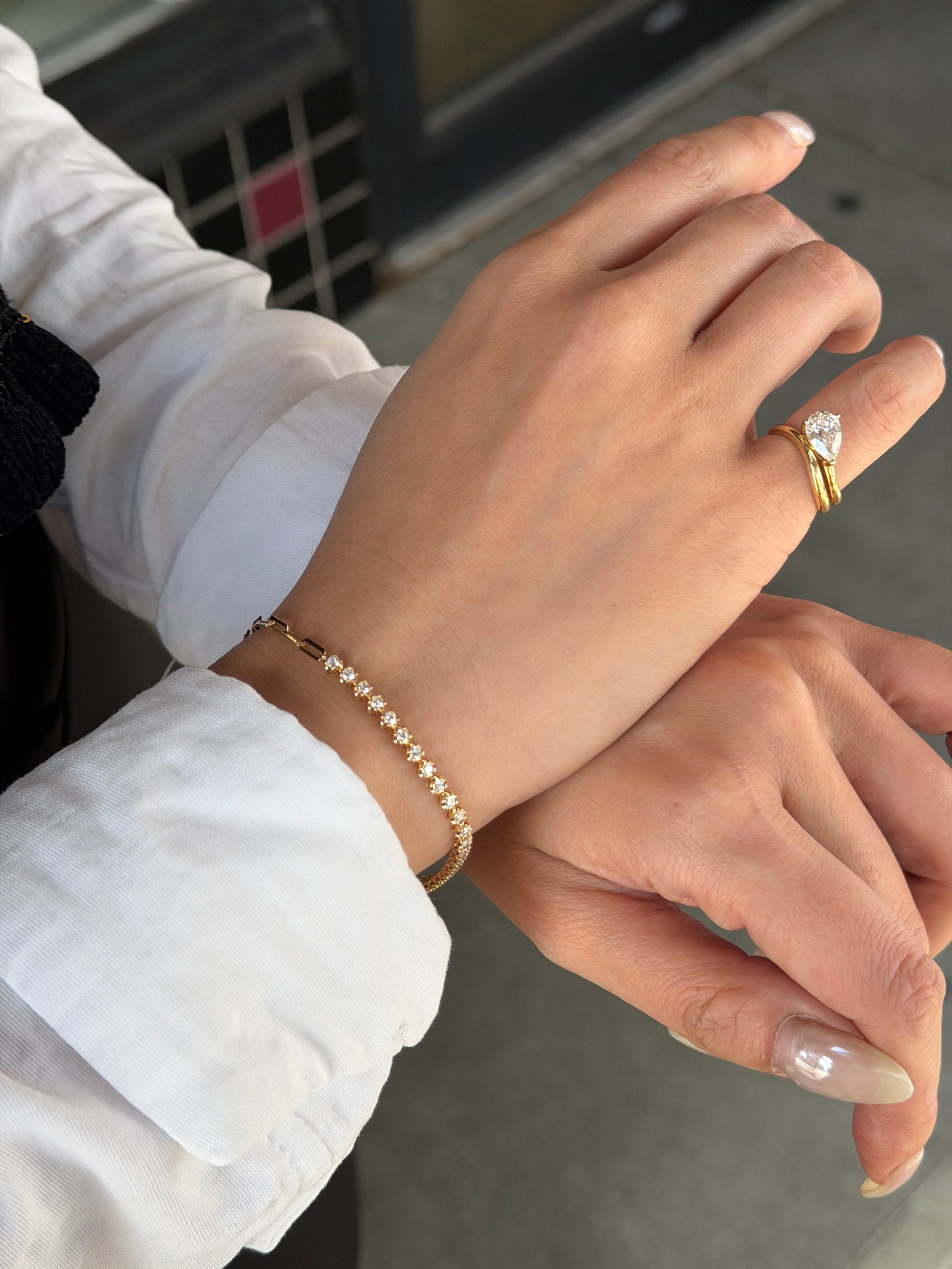 A model showcasing the 18K Natural Diamond Half Paperclip & Tennis Bracelet on her wrist, paired with a stunning pear-shaped diamond ring worn on the hand. The yellow gold jewelry set is styled elegantly against a white collared shirt, perfect for everyday luxury.
