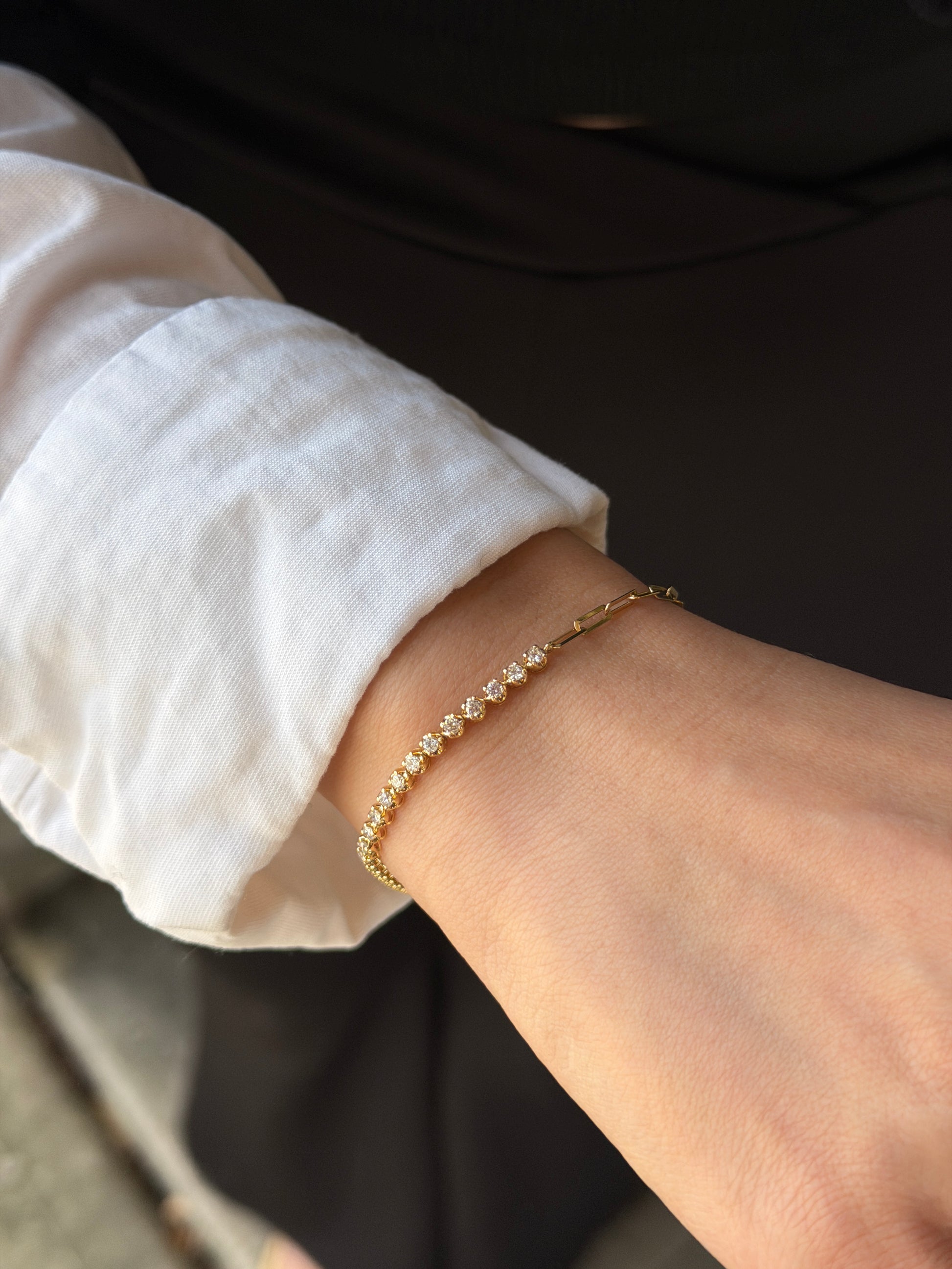 A model wearing the 18K Natural Diamond Half Paperclip & Tennis Bracelet in yellow gold, styled with a crisp white shirt. This modern fine jewelry piece features a seamless hybrid design, transitioning from a classic row of brilliant-cut diamonds to sleek gold paperclip chain links.