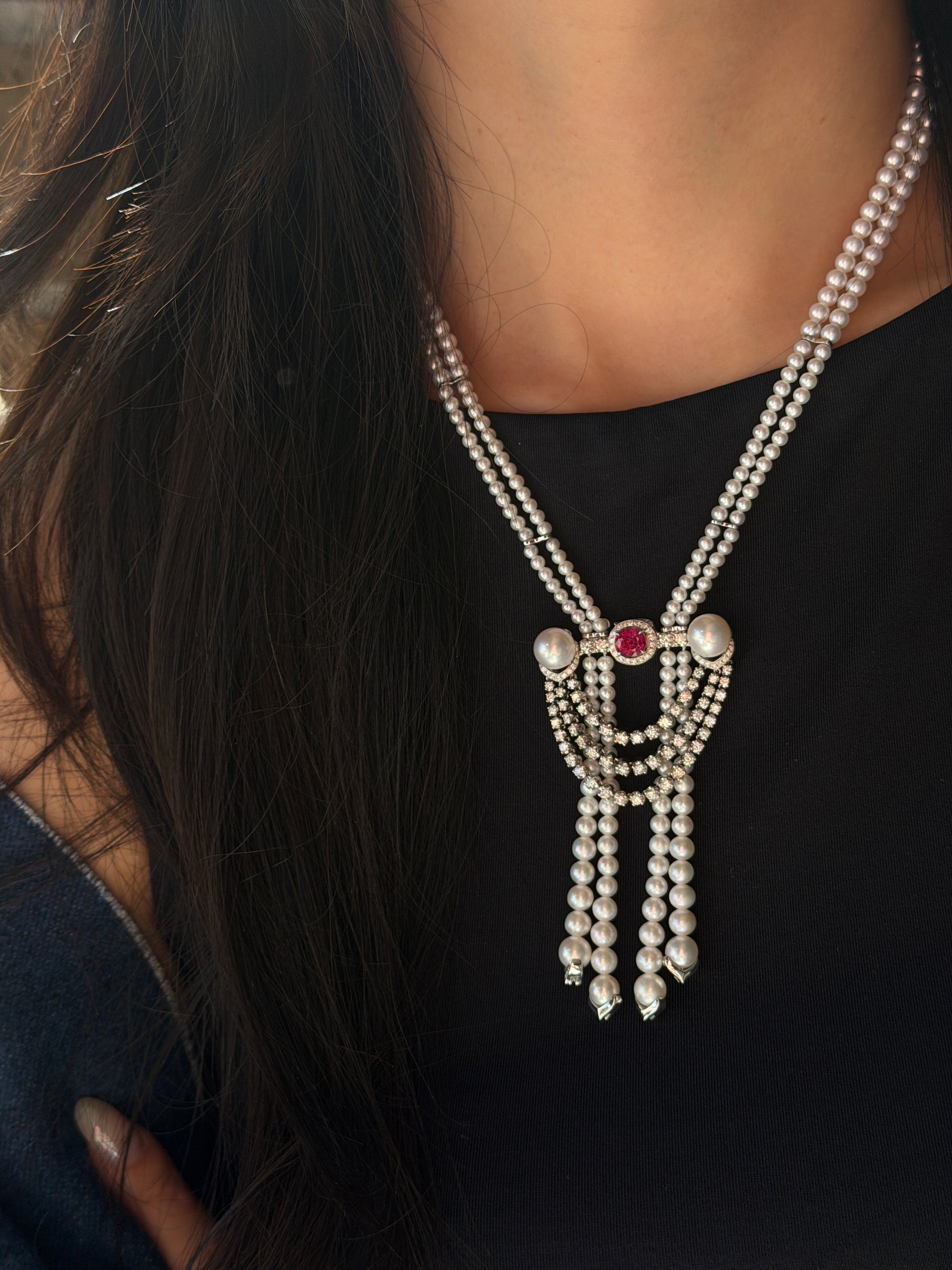 A model wearing a luxurious double-strand Akoya pearl necklace featuring a versatile centerpiece brooch. The intricate brooch in IMG_0810.jpg showcases a 1.16ct ruby surrounded by a diamond halo, flanked by two large pearls, with cascading diamond swags and three Akoya pearl tassel drops.