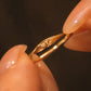 Macro photography of fingers holding an 18K gold ring, revealing the custom secret initial MY engraved on the inner band.