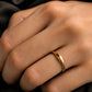 Close-up of a sleek, glossy 18K gold matching ring with a curved modern wave design worn on a woman's hand.