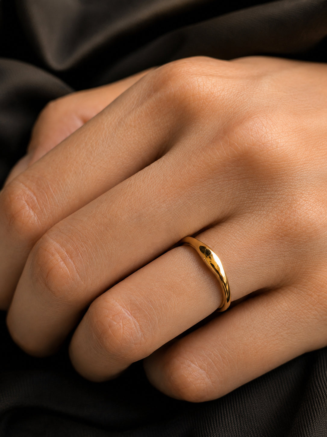 Close-up of a sleek, glossy 18K gold matching ring with a curved modern wave design worn on a woman's hand.
