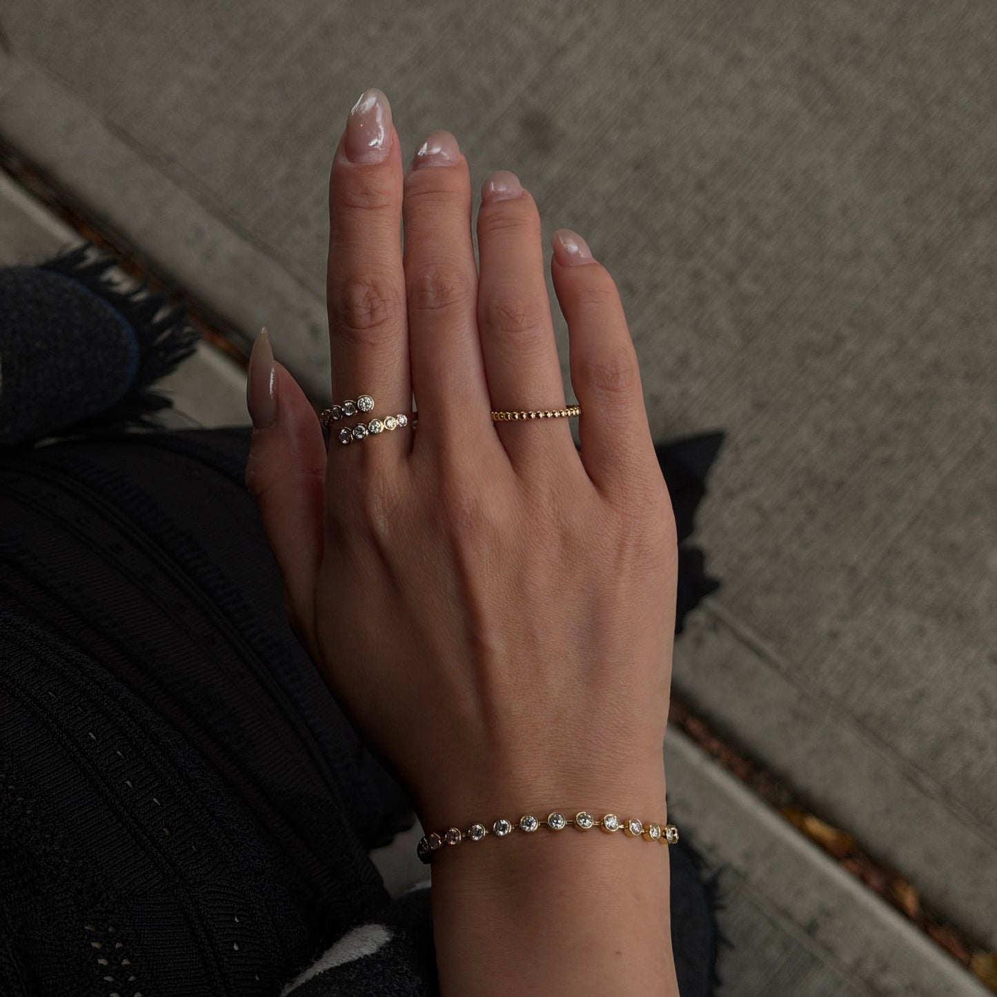 Top-down view of a woman's hand wearing an 18K gold bezel-set lab-grown diamond wrap ring outdoors.