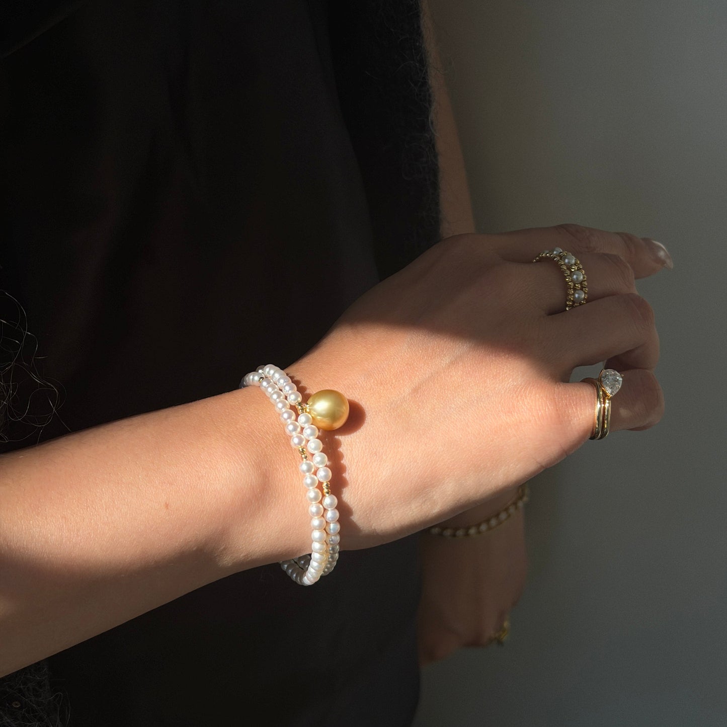 A double-strand white pearl wrap bracelet featuring a large golden pearl in the center and small gold beads, shown on a white background.