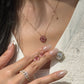 A close-up of a woman wearing an 18K natural ruby floral pendant necklace on a delicate gold chain, while holding a matching pair of ruby floral stud earrings.