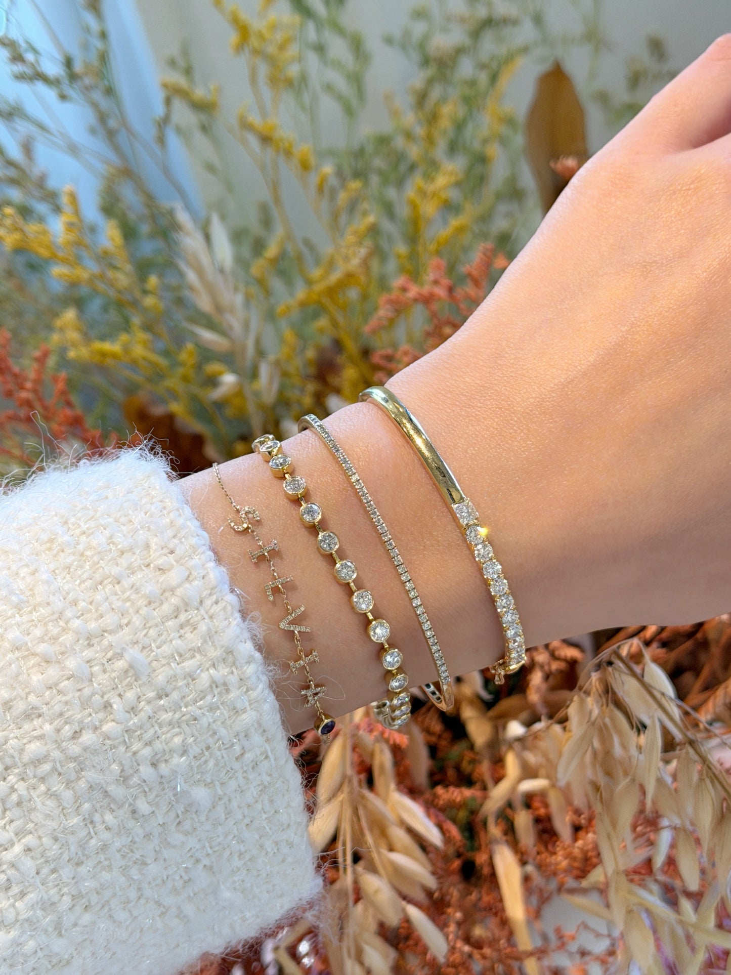 A close-up of a wrist adorned with a sophisticated stack of four gold and diamond bracelets/bangles, featuring the Fantasilvia 18K Half-Eternity Diamond Bangle.