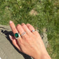Hand wearing an 8.52 carat natural green tourmaline ring with diamond halo, blue sapphire accents, and an 18K gold setting, styled outdoors in natural sunlight.