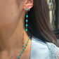 A close-up of a woman's side profile, focusing on her ear and neck. She is wearing a long dangle earring featuring bright blue Persian turquoise beads connected by gold chain links, alongside a small diamond hoop in a second piercing. The matching Persian turquoise and gold bead necklace is visible around her neck. She is wearing a light blue shirt.