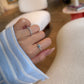 A close-up of a hand modeling two rings in a bright, modern boutique setting. The index finger features a classic diamond band, while the ring finger showcases a dainty ring with a horizontally set rectangular light blue gemstone on a thin diamond pavé band.