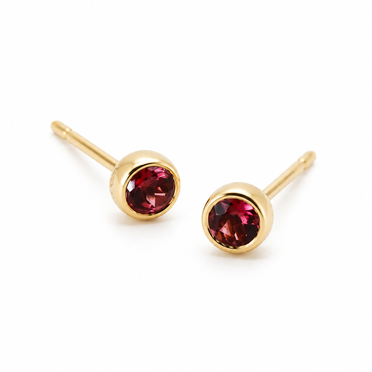 Pair of 18K yellow gold stud earrings featuring bezel-set round deep red garnet gemstones.