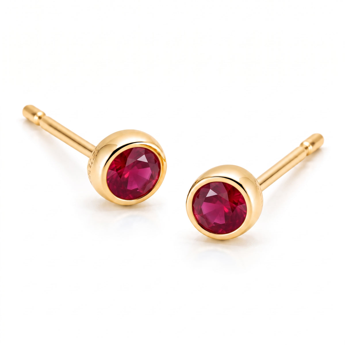 Pair of 18K yellow gold stud earrings featuring bezel-set round red ruby gemstones.