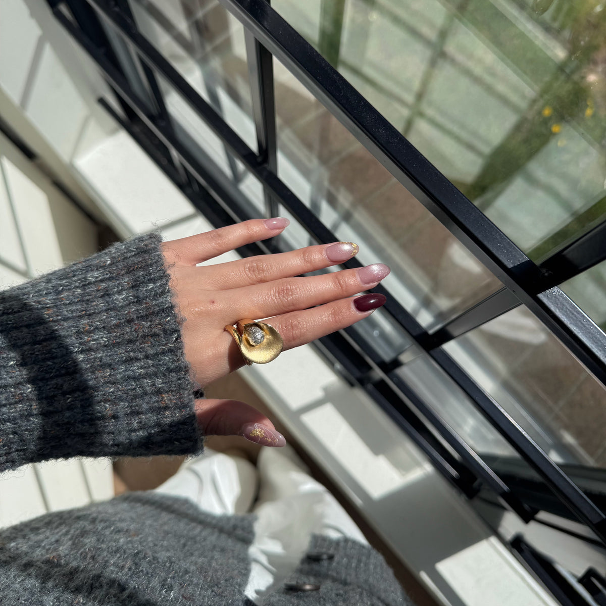 Italian silver statement ring featuring a sculptural gold-tone swirl design with a textured silver center, styled on the hand in natural sunlight.